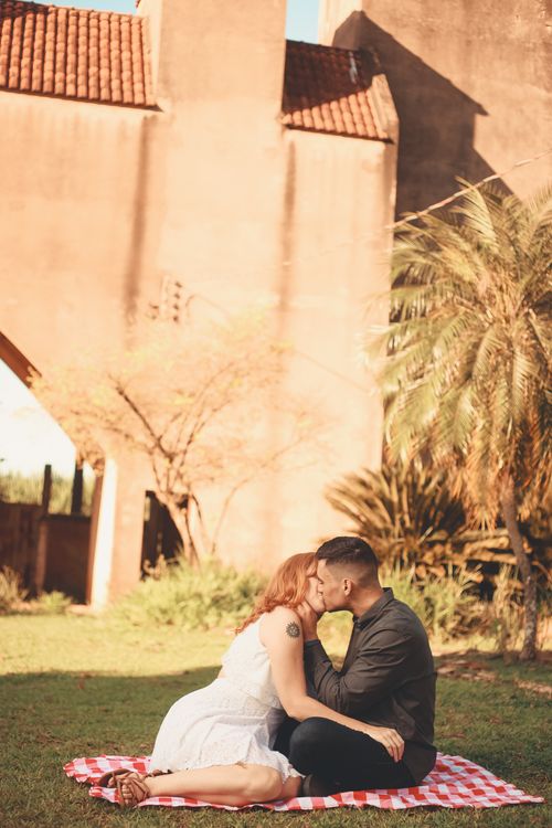Free A couple shares a romantic kiss while sitting on a blanket outdoors during a sunny day. Stock Photo