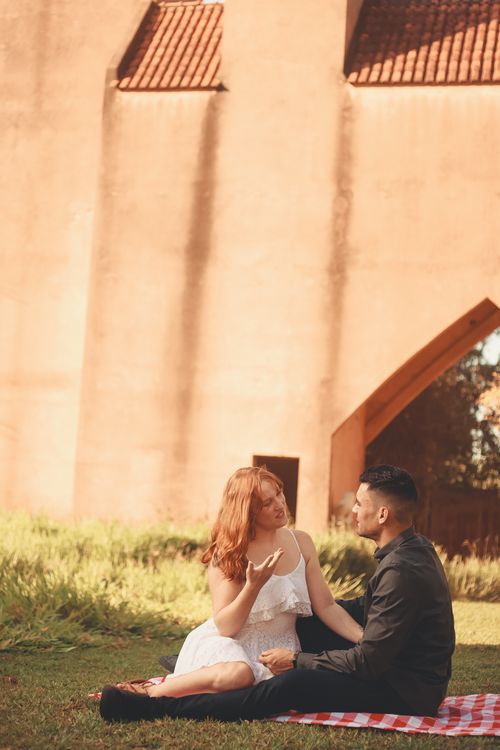 Free A couple enjoying a romantic picnic sitting on a blanket near a wall in daylight. Stock Photo