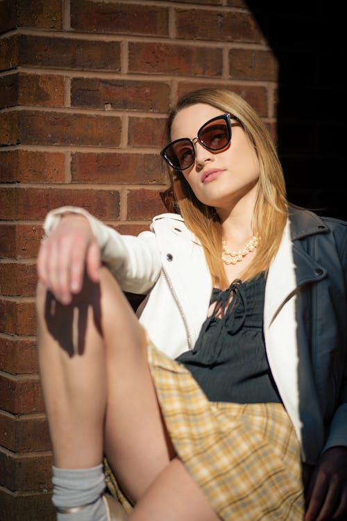 Woman in a Jacket and a Tartan Skirt Sitting Against a Brick Wall