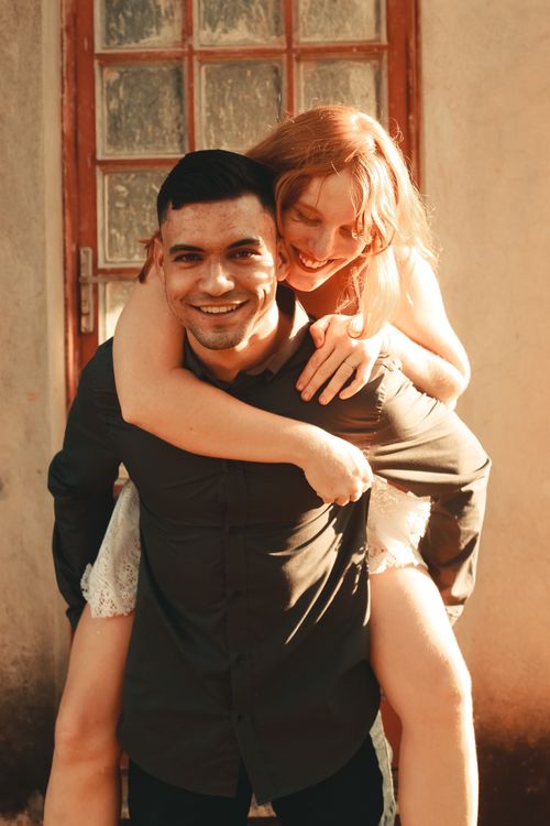 Free Smiling couple sharing a joyful moment with a piggyback ride in a warm, sunny setting. Stock Photo