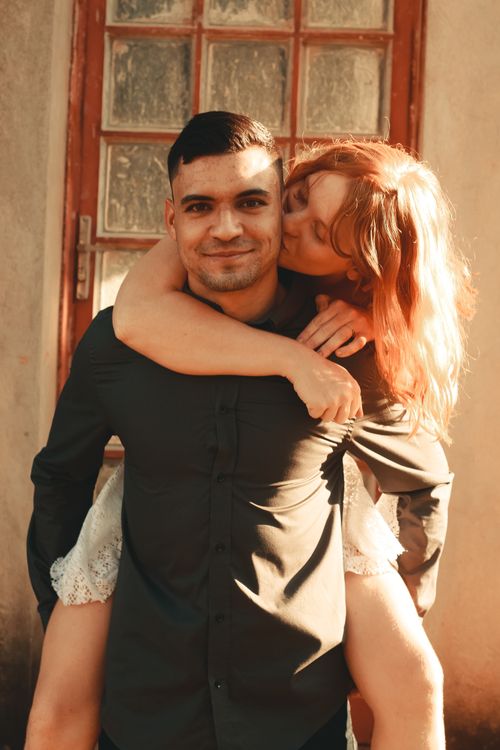 Free A cheerful man gives a piggyback ride to a smiling woman, captured outdoors in warm light. Stock Photo