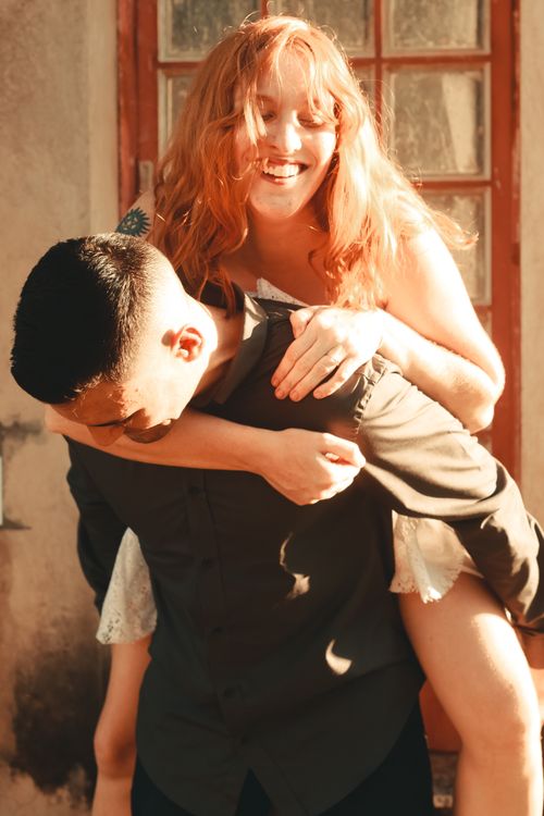 Free Laughing couple enjoying a fun piggyback ride in the sunlight, showcasing happiness and togetherness. Stock Photo