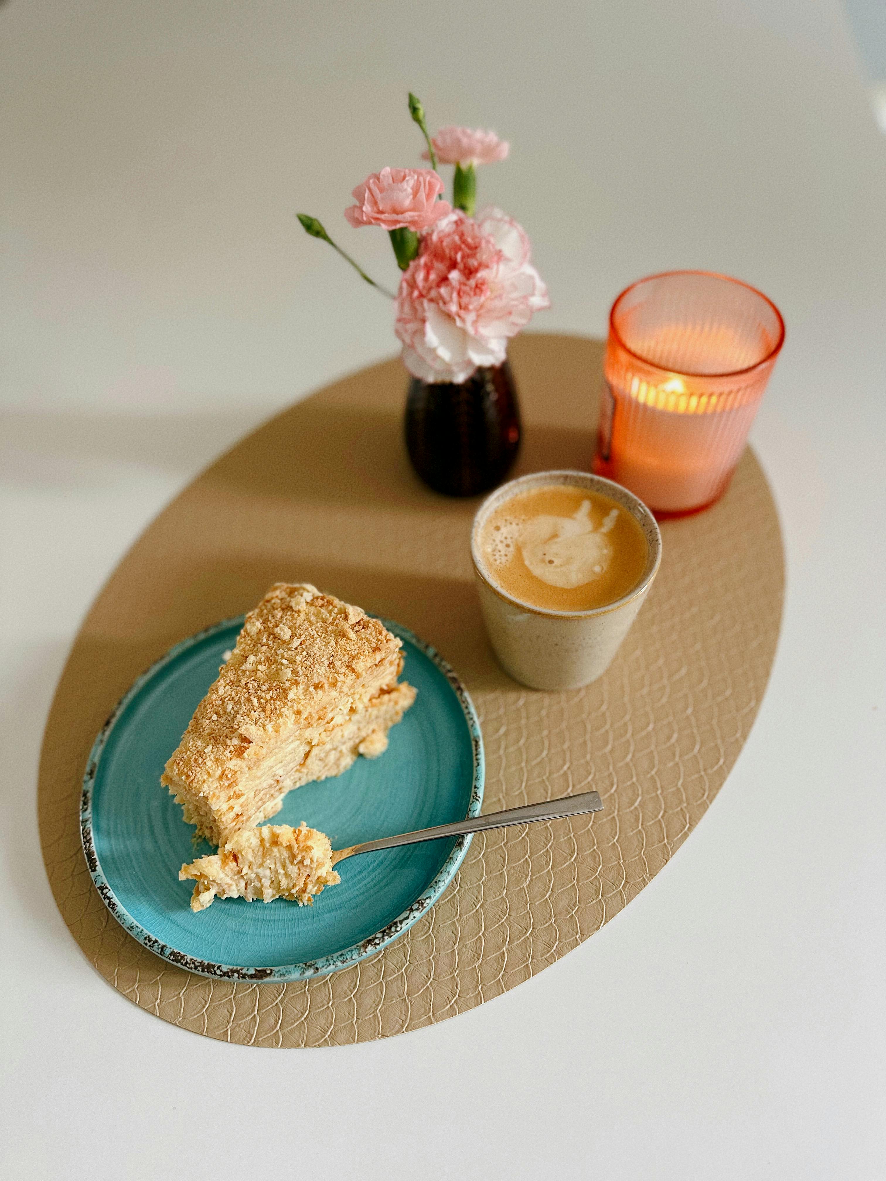 A tranquil scene featuring cake, coffee, flowers, and a candle on a styled table setup.