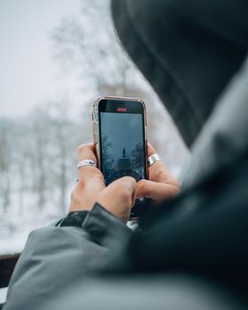A person capturing a winter scene in Kyiv, Ukraine, using a smartphone amidst snowy trees.
