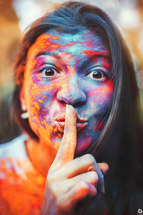 Free Portrait of a woman joyfully covered in colorful Holi powders, making a shushing gesture. Stock Photo