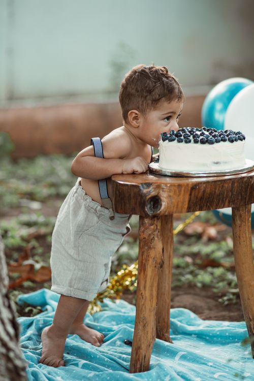 Free A young child leans over to taste a blueberry cake during an outdoor birthday celebration. Stock Photo