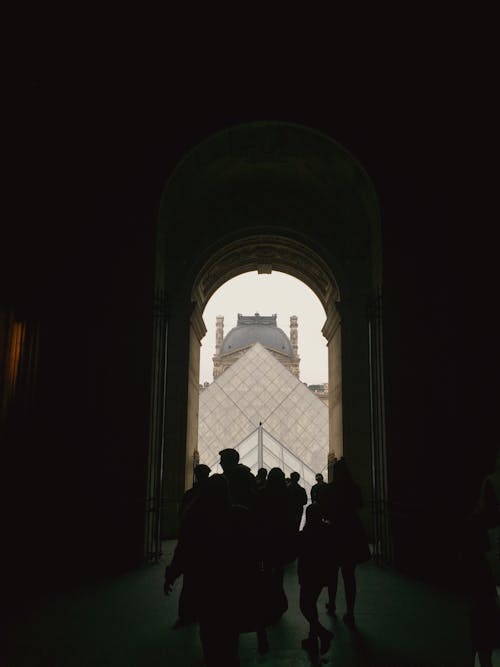 Silhouettes of People Walking in an Arcade with View of the Louvre in Paris, France 