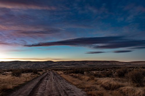 Free Beautiful dirt road at sunset with vibrant sky and hills. Perfect for nature and outdoor themes. Stock Photo