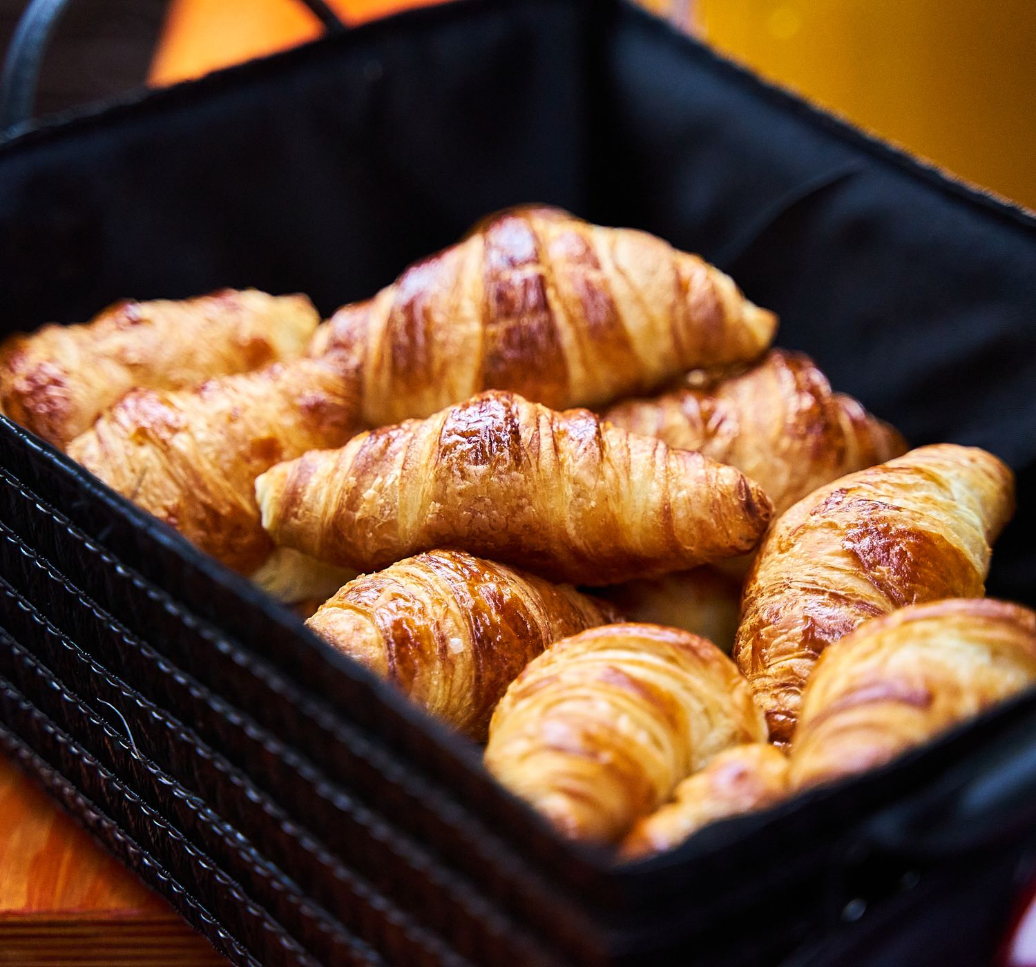 A closeup of fresh croissants in a black basket, perfect for breakfast or brunch.