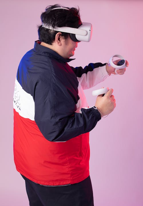 Man in a Jacket Wearing a VR Headset and Holding the Controllers