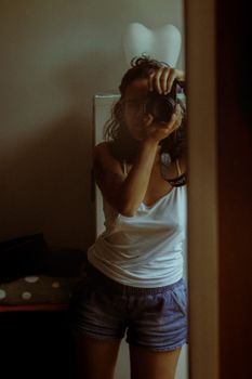 A woman capturing her reflection in a room mirror with a camera.