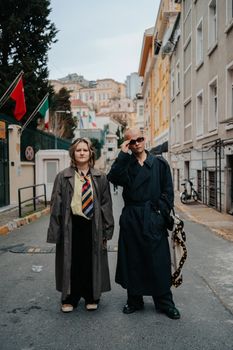 Two people in stylish attire pose confidently on a city street, showcasing modern urban fashion.