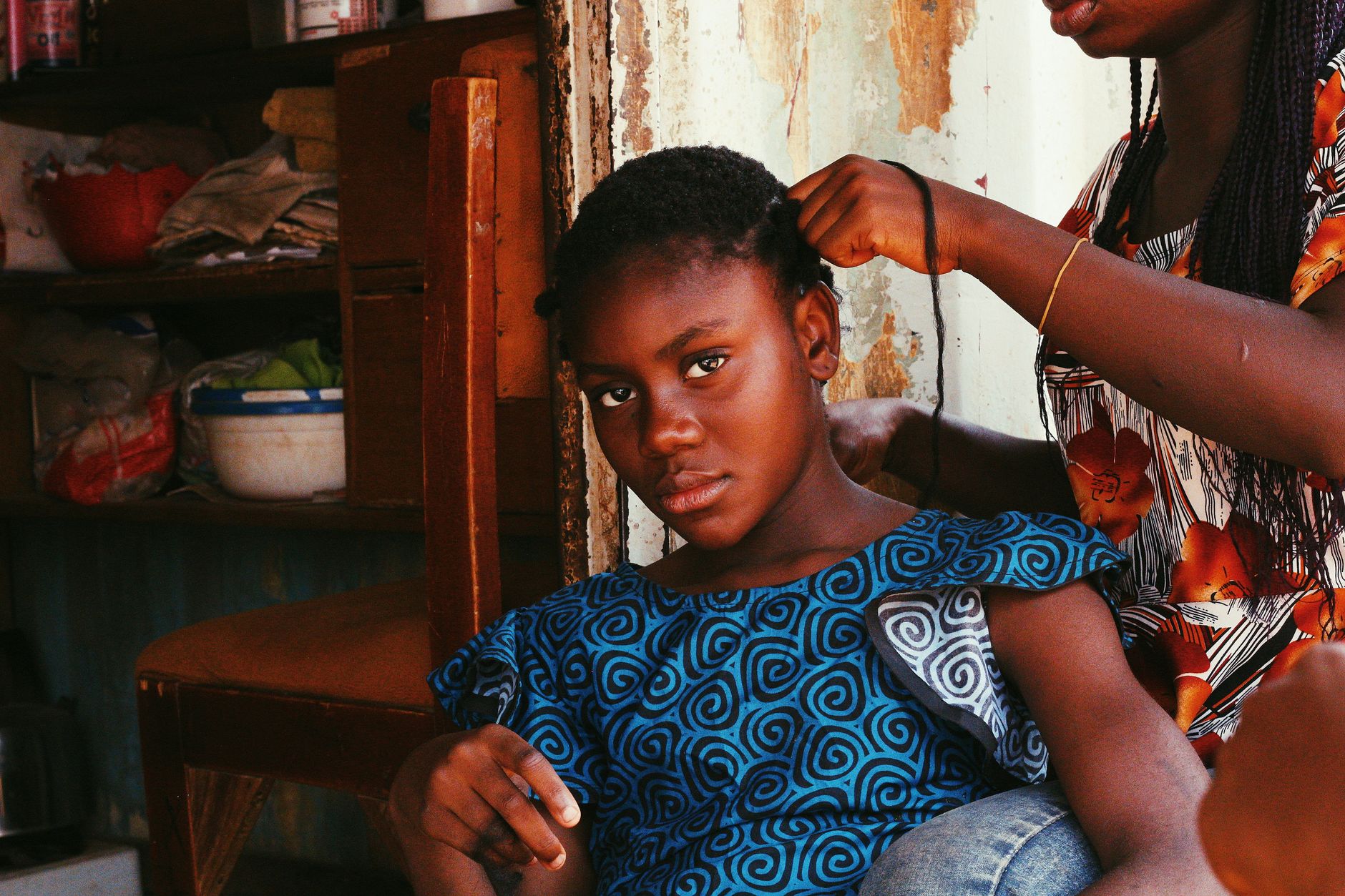 A young girl gets her hair braided indoors in Abuja, Nigeria.
