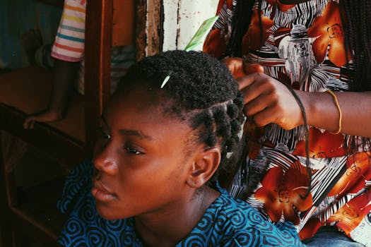 A young African girl getting her hair styled, captured in Abuja, Nigeria.