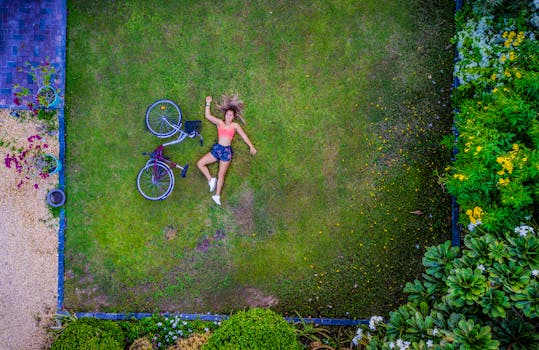Aerial shot of a woman lying on a lawn with a bicycle in a garden setting in Dubai.