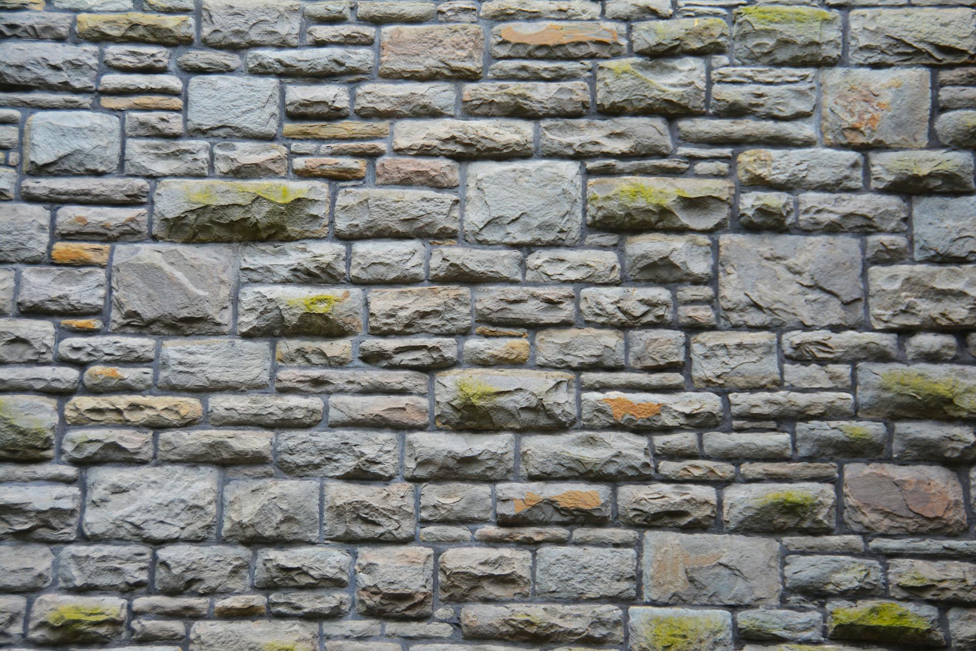 Close-up of a textured stone wall with moss, showcasing natural patterns and rugged appeal.