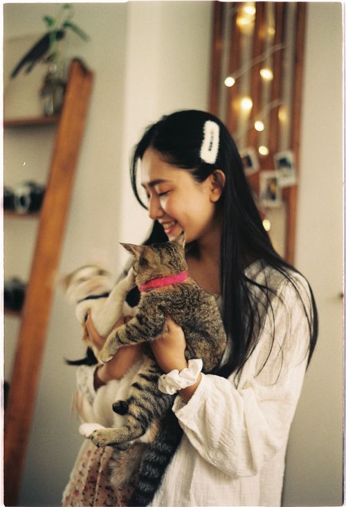Free Young woman happily holding two cats indoors with warm lighting. Stock Photo