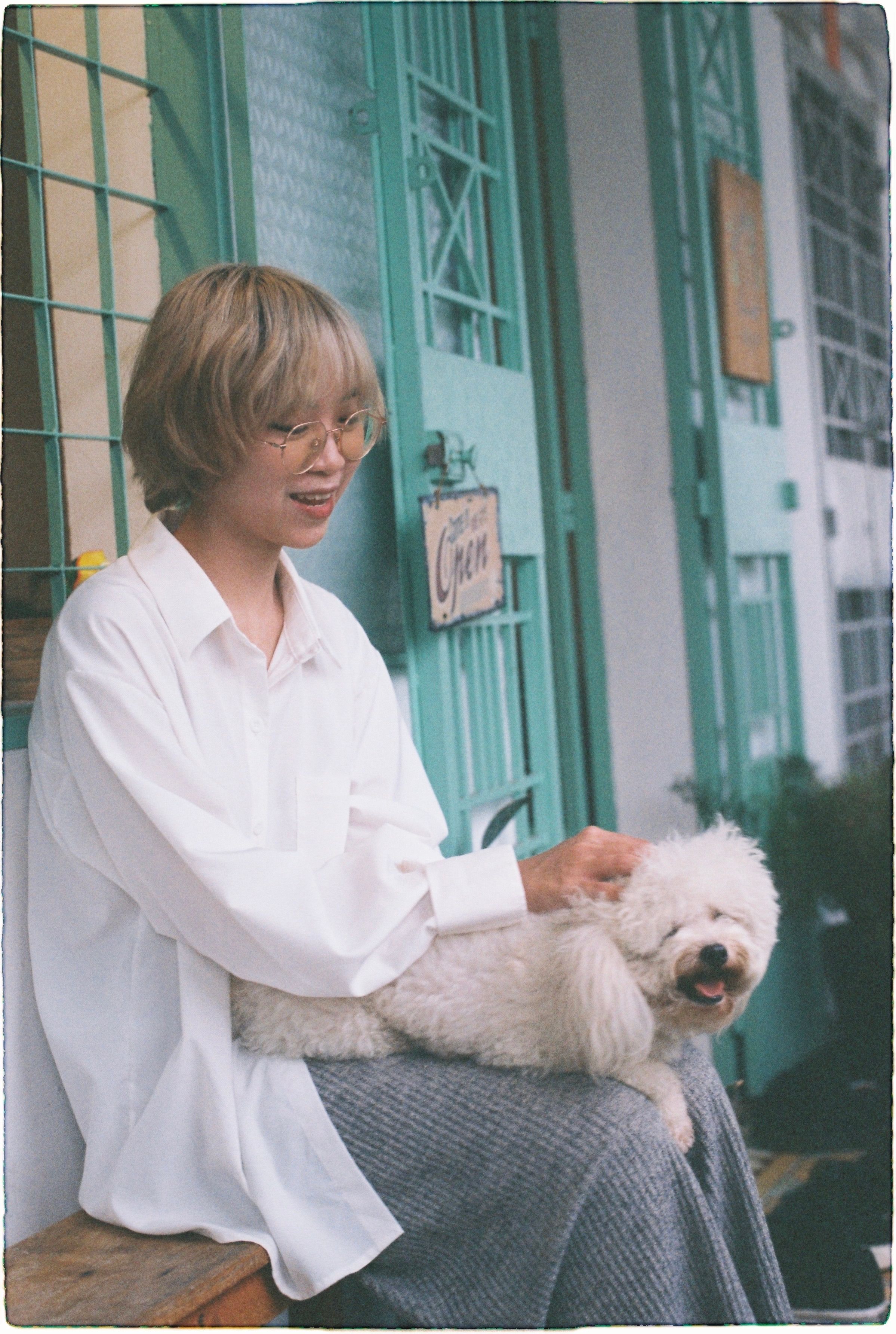 A woman sits on a bench petting a happy dog outside an urban building.