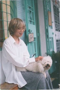 A woman sits on a bench petting a happy dog outside an urban building.