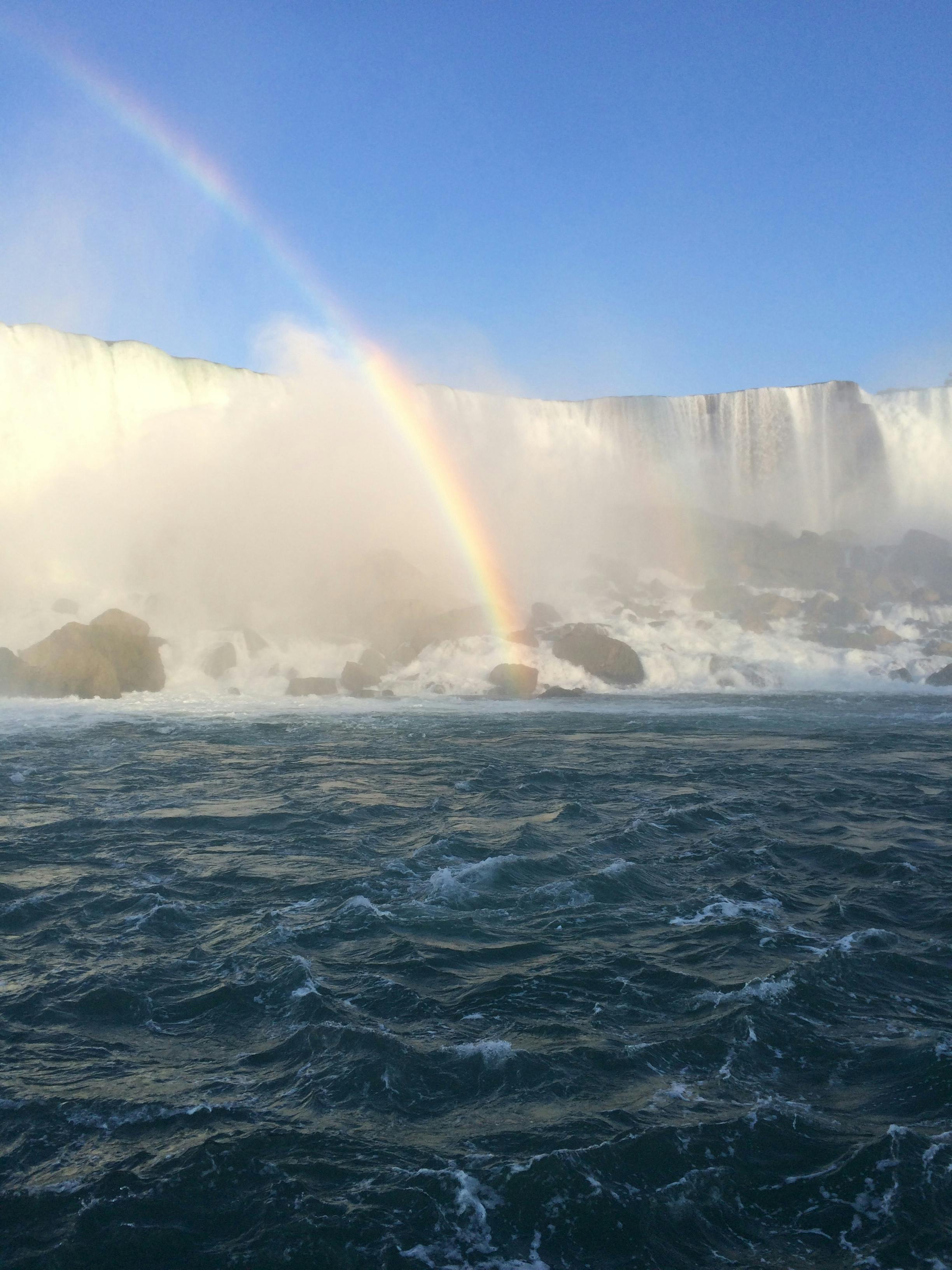 Breathtaking view of a rainbow arching over a powerful waterfall on a clear day.