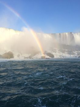 Breathtaking view of a rainbow arching over a powerful waterfall on a clear day.