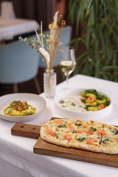 Inviting Italian dining setup with fresh pizza, pasta, and white wine on a stylish table.