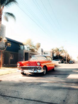 A classic red vintage car parked on a sunny residential street lined with palm trees.