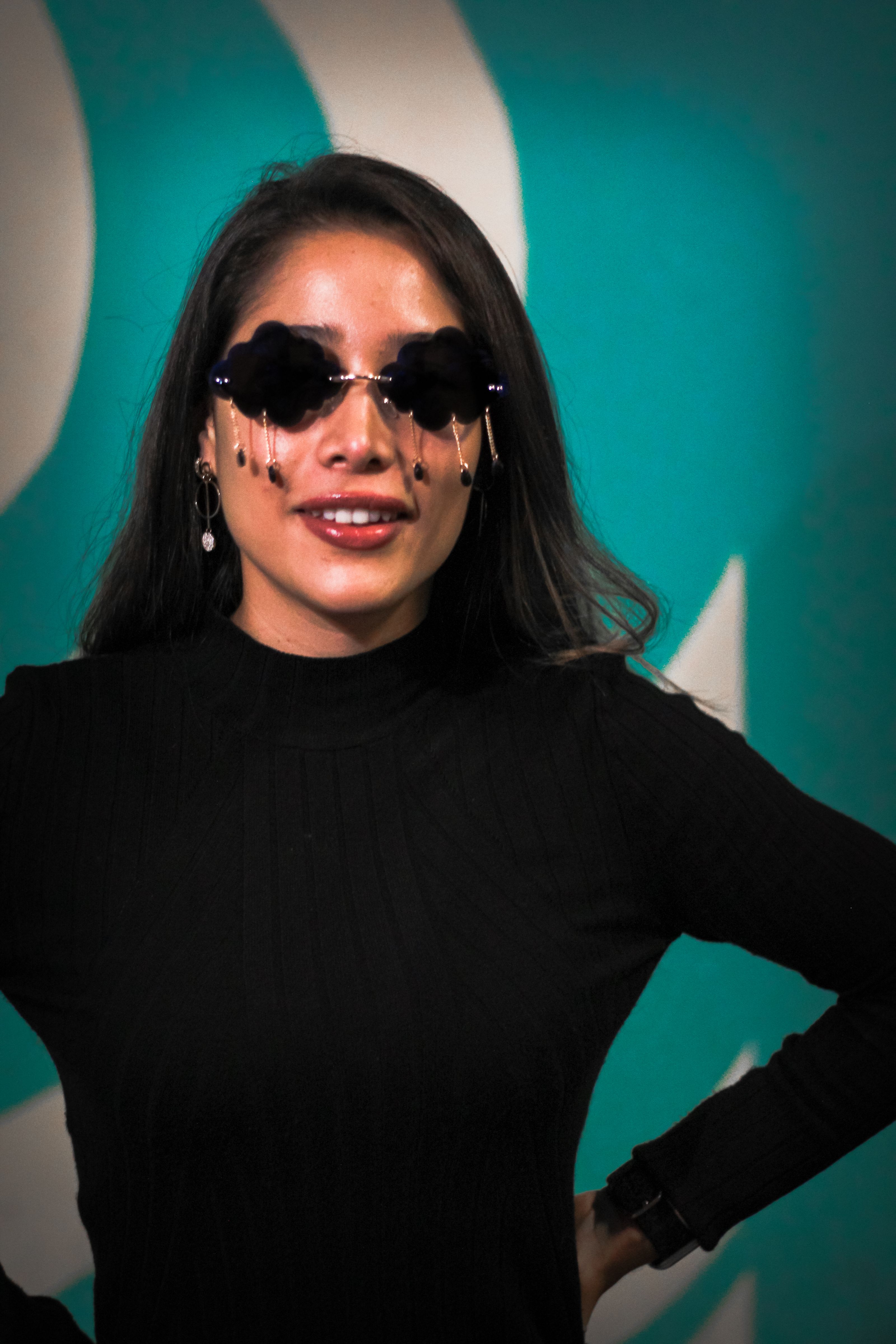Mulher da moda em suéter preto posando em ambientes internos com óculos de sol únicos.