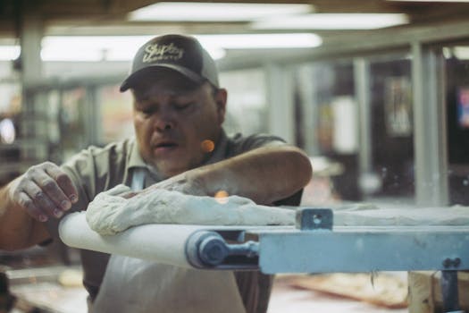 Male baker in a bakery shop preparing dough on a rolling machine indoors.