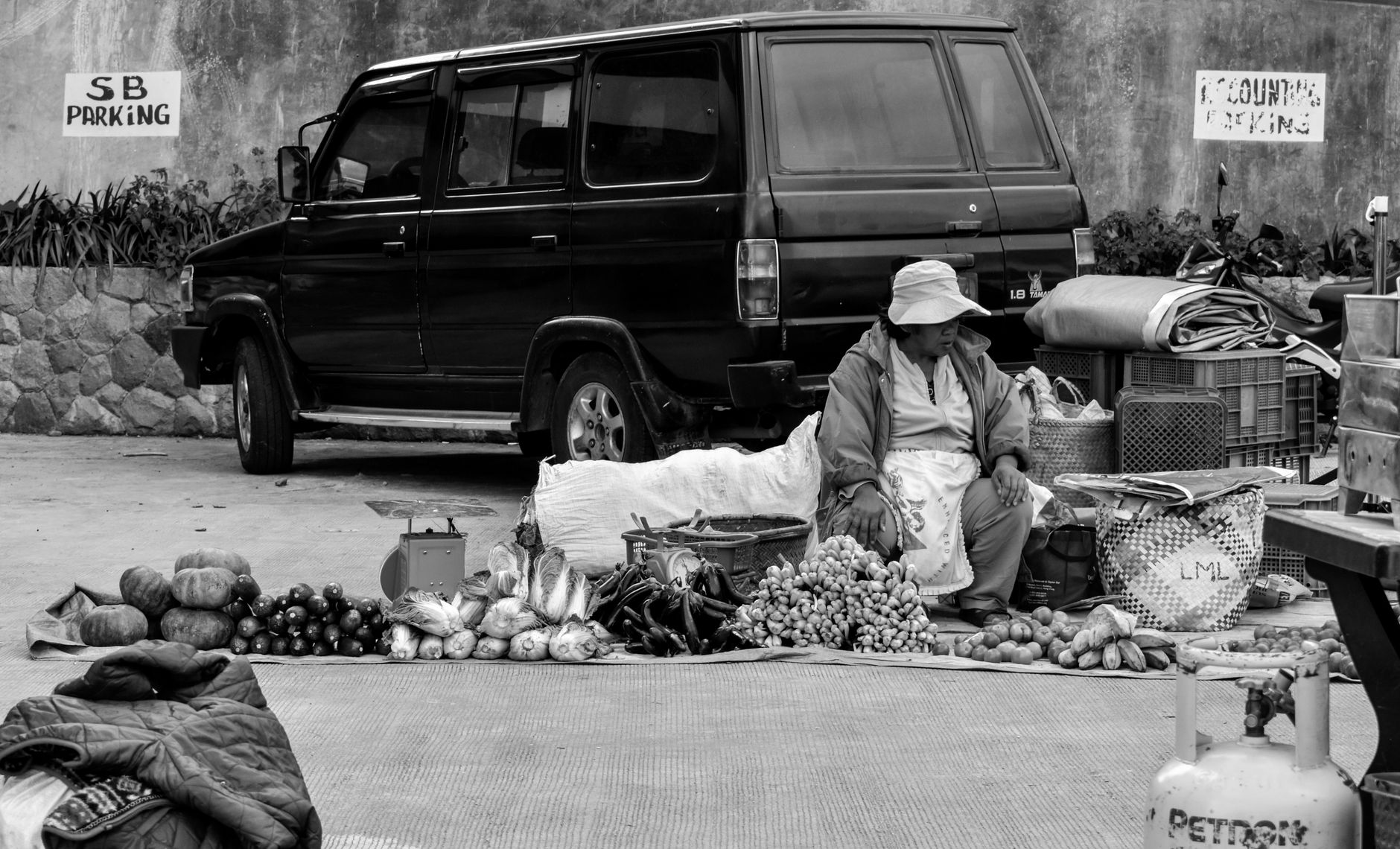 A street vendor in the Philippines selling fruits and vegetables beside a parked vehicle.