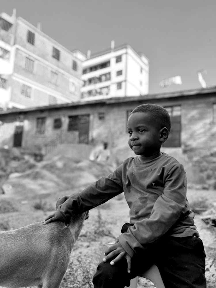 Black And White Photo Of Young Boy Sitting In Rubble Petting Dog