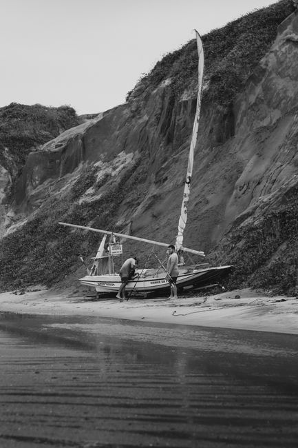 Two men with sailboats near cliffs on Canoa Quebrada beach in Brazil.