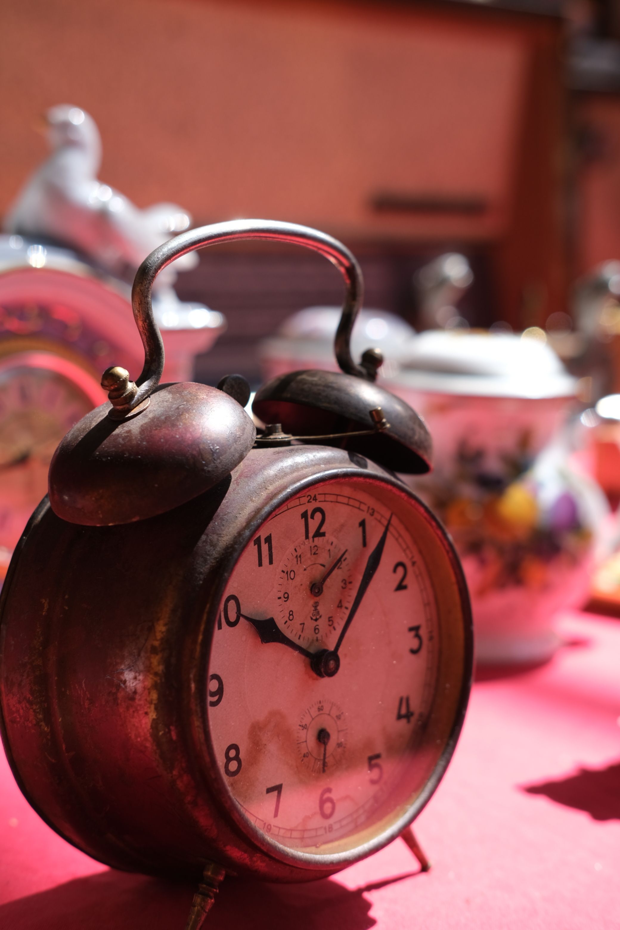 Close-up of a vintage alarm clock surrounded by assorted antique teaware, capturing a classic and nostalgic mood.