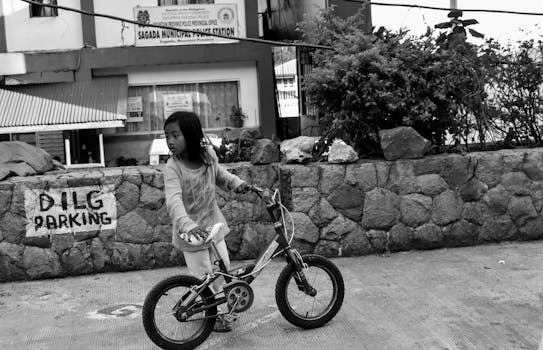A young girl riding a bicycle outside Sagada Police Station. Black and white street photo.