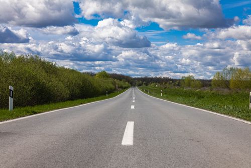 Free Open countryside road stretching into the horizon under a sky filled with dramatic clouds. Stock Photo