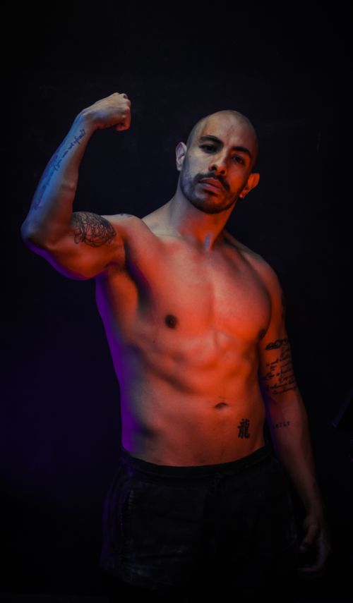 Free Shirtless muscular man with tattoos posing confidently in dramatic studio lighting. Stock Photo