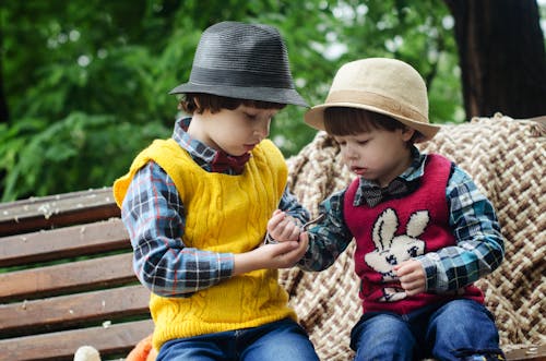 帽子と長袖のシャツを着てベンチに座っている2人の男の子