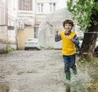穿着黄背心的男孩在雨天撑着伞，在水坑里玩耍