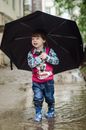 一个快乐的孩子穿着毛衣和雨靴，撑着黑伞在外面玩耍