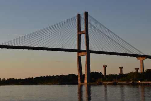 Free A stunning suspension bridge spans a serene river, captured at sunset. Stock Photo