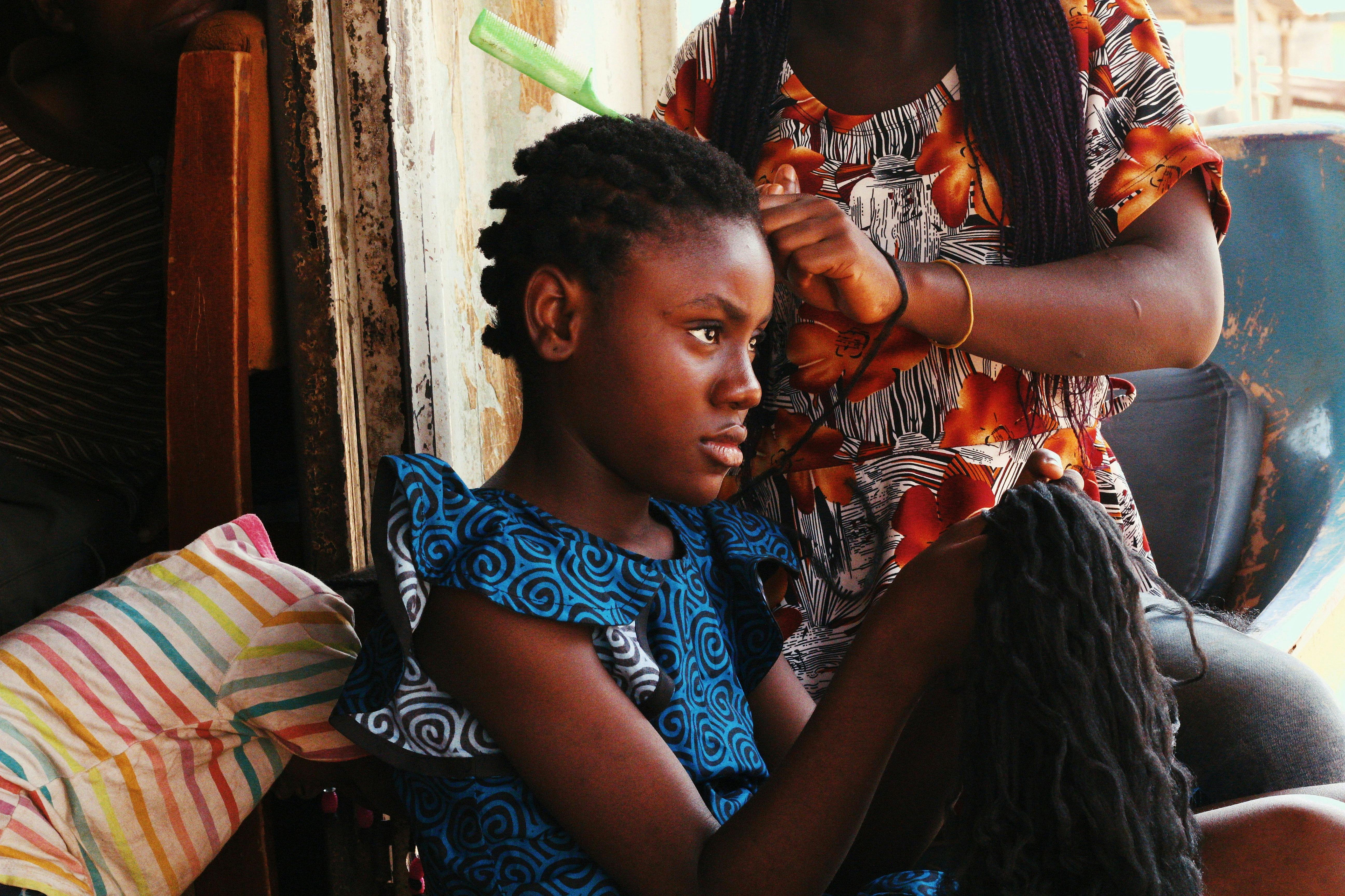 A Nigerian girl gets her hair braided at home, showcasing cultural hair styling.