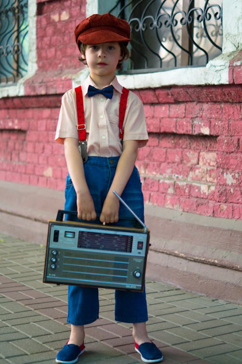 Foto Des Jungen, Der Radio Hält Und Neben Dem Roten Haus Steht