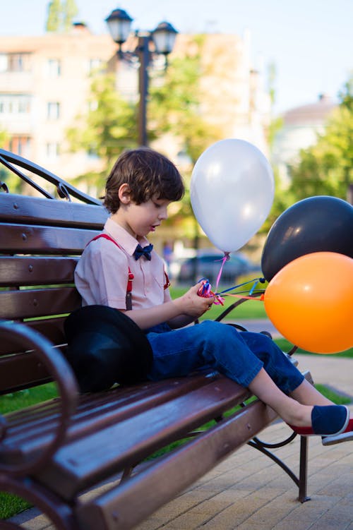 Free Boy Sitting On Bench While Holding Balloons Stock Photo