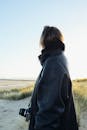 穿着皮夹克的女人在白天拿着相机站在海边