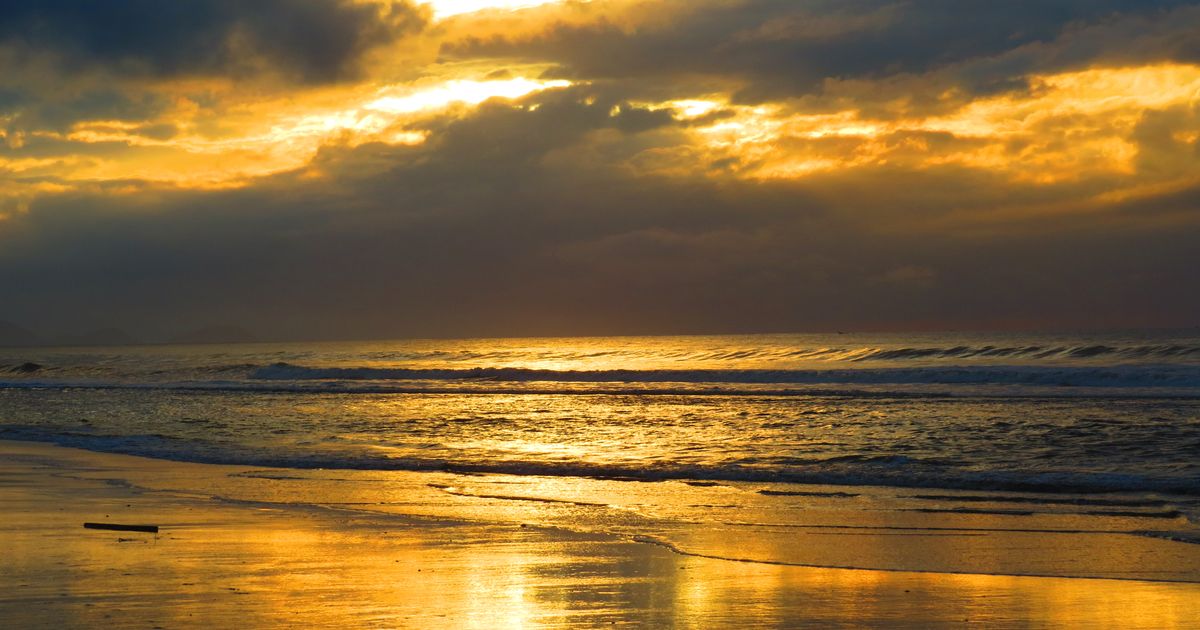 Um pôr do sol deslumbrante sobre uma praia tranquila com reflexos dourados na água.