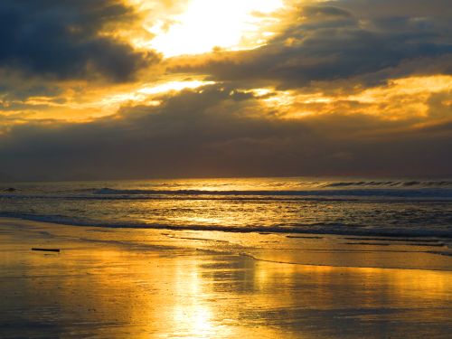 Free A breathtaking sunset over a tranquil beach with golden reflections on the water. Stock Photo
