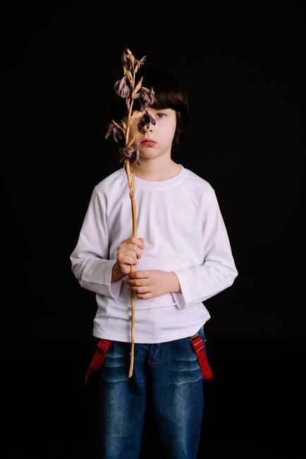 Portrait of a young boy in casual wear holding dry leaves against a black studio background.