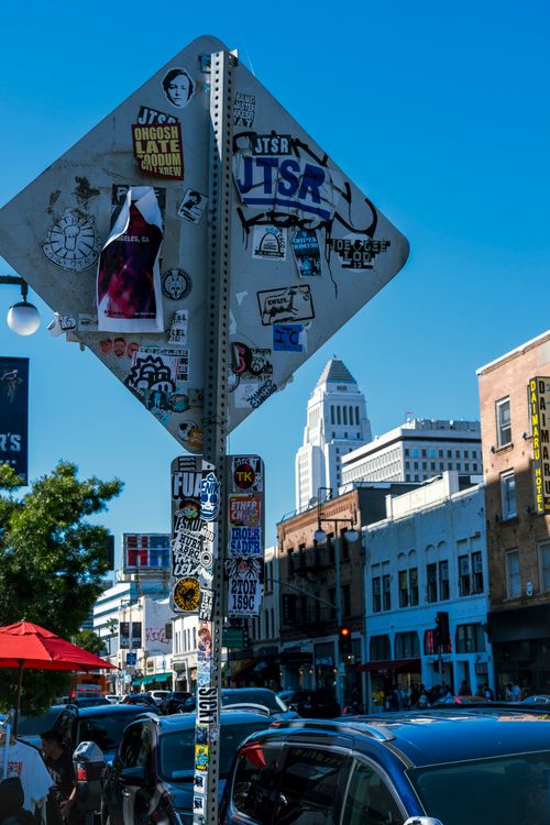 Free Vibrant city street view featuring a sticker-covered road sign and skyscrapers under blue skies. Stock Photo