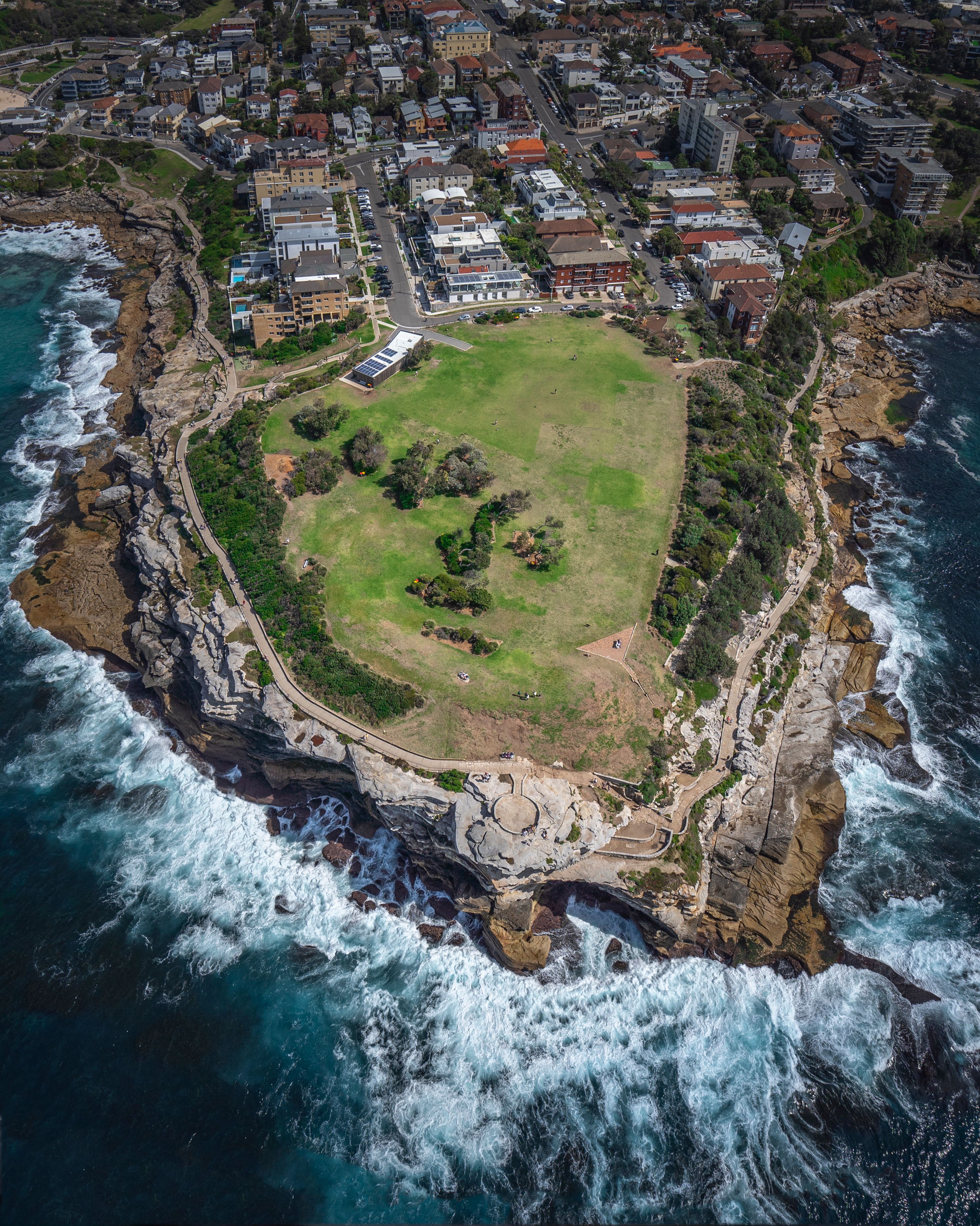 A stunning aerial photograph showcasing a coastal town and lush park surrounded by waves.