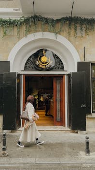 A woman in hijab walks into a café, carrying a bouquet, in an urban setting.